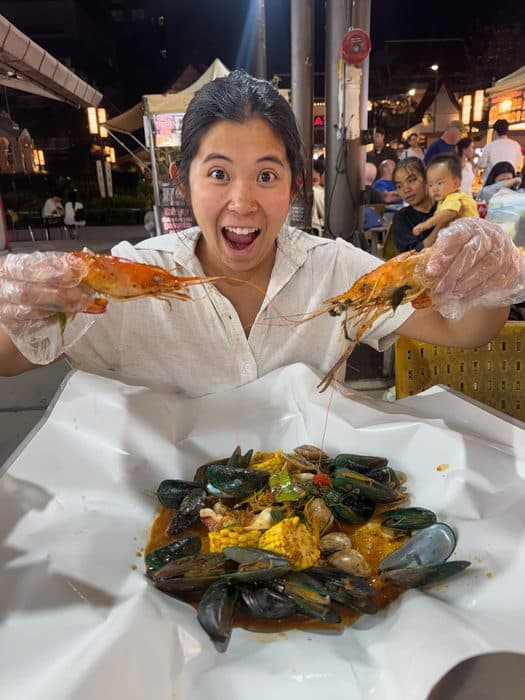 Jenny holding two prawns over a seafood boil at a night market