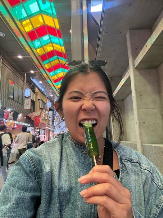 Jenny with a pickled cucumber on a stick in an Osaka arcade