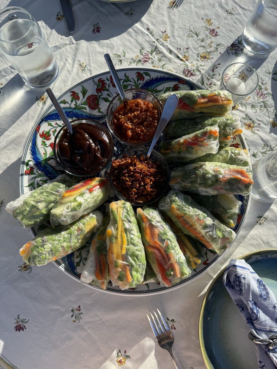 Fresh spring rolls fanned around four dipping sauces on a painted platter